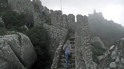 The writer descends from one of the towers of the Castelo dos Mouros, overlooking Sintra in Portugal, with Pena Palace peeking out of the clouds in the background.