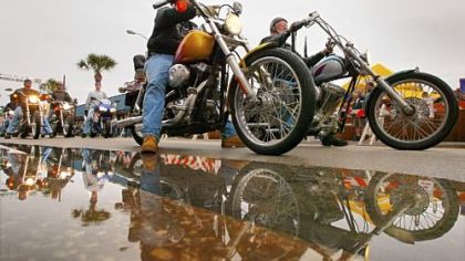 Bikers are reflected in water left behind on Main Street by rain showers during Bike Week in Daytona Beach, Fla.