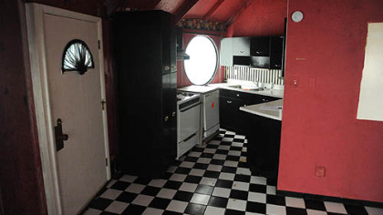 The compact kitchen has bright-red walls, black wood cabinetry and a vintage black-and-white checkered linoleum floor.