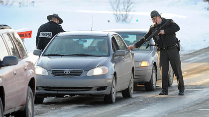 Two Pennsylvania State Police troopers search cars coming from Bredinsburg Road as part of a manhunt for the man who killed a fellow state trooper.