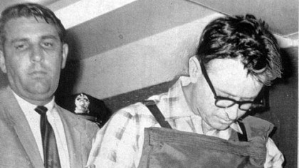 James Earl Ray, manacled and wearing a bullet-proof vest and heavy safety pants, is led to his four-cell Memphis suite by Shelby County Sheriff William Morris in July 1968.