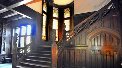 Light from stained glass windows casts a warm glow on the carved quartersawn oak wainscoting and staircase in the grand hall.