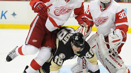 Penguins forward Tyler Kennedy is knocked to the ice by Red Wings defenseman Brad Stuart in front of goaltender Chris Osgood.