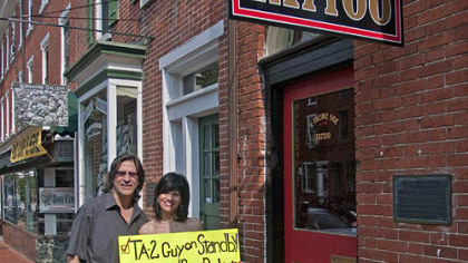 Rose Ann Belluso and her husband, Jim, stand in front of X-Treme Ink Tattoo in West Chester, Pa., with the sign Rose Ann used to get her back signed by Paul McCartney during a concert Sunday night in Philadelphia.