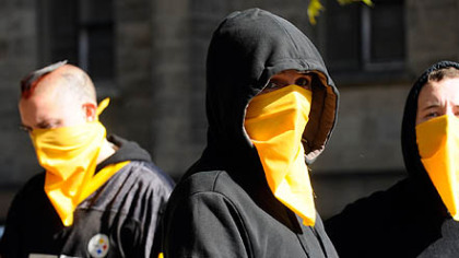 Two dozen people, many covering their faces with gold bandanas, protested Ben Roethlisberger's return to the Steelers by marching from the National Aviary to Heinz Field.