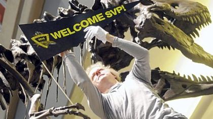 Perching on top of a 10-foot ladder, Dan Pickering of the Carnegie Museum of Natural History adjusts a sign in the claw of the Tyrannosaurus rex on display at Pittsburgh International Airport. The sign welcomes the members of the Society of Vertebrate Paleontologists to its 70th annual meeting.