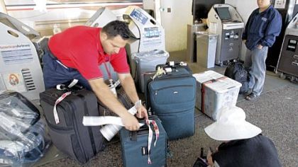 An American Airlines luggage handler helps passengers check in luggage Friday at San Jose International Airport. American Airlines said it planned to charge passengers $15 for the first checked bag.