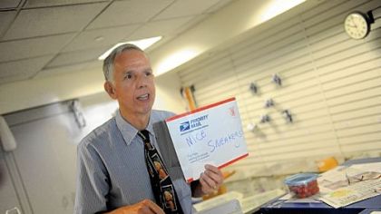 Mike Herr holds up a sign that reads "Nice Sneakers" to the next person in line at the University Park post office.