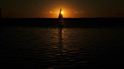 A sailboat launches from a dock at Dobbins Landing on Lake Erie at sunset.