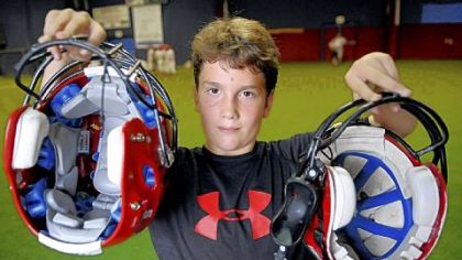 Nick Young, 10, holds a $150 Schutt helmet in his right hand and a regular helmet in his left. He was wearing the family-purchased Schutt hel-met when he sustained a concussion. The helmet is designed to prevent catastrophic head trauma.