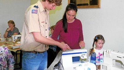 Noah Pillion-Gardner teaches Bonnie and Josie Dougherty how to make Cool Ties. The ties, which soldiers wear around their necks to beat the heat, are Noah's Eagle Scout project.